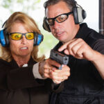 A firearm shooting instructor assisting a student at a shooting range.